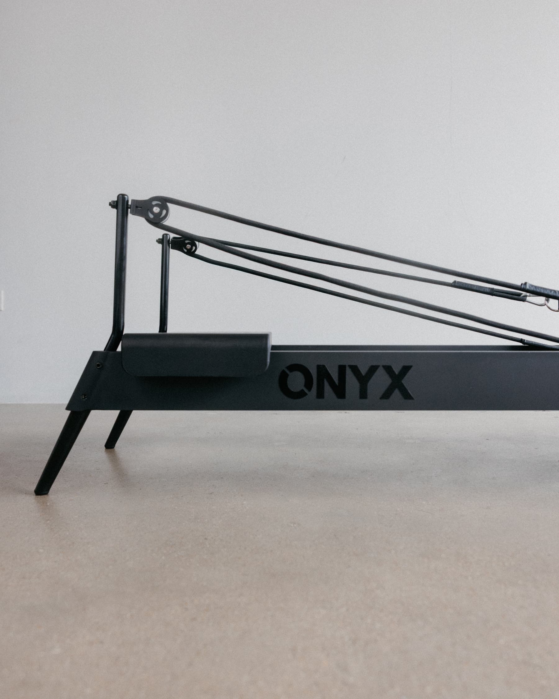 The proprietary ONYX reformer, matte black with the ONYX wordmark cut into the frame, on a pale studio floor.