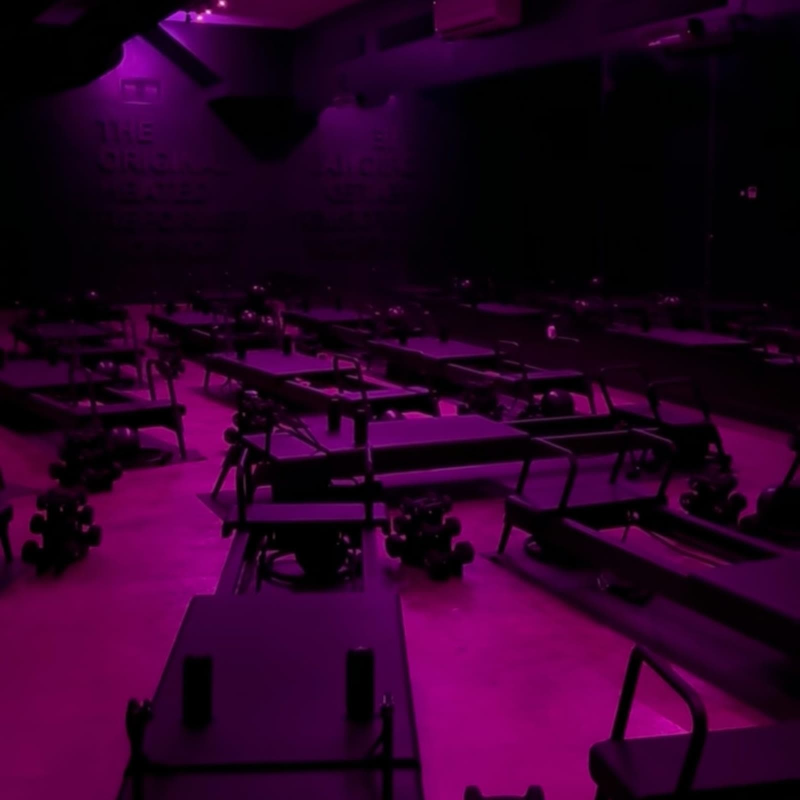 An empty ONYX studio floor, reformers in formation under the magenta house lights before class.